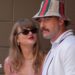 Taylor Swift, wearing a red gingham top, looking up at Travis Kelce, wearing a striped Gucci bucket hat