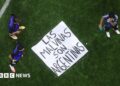 A banner saying "Las Malvinas Son Argentinas" is on the ground of a pitch with three players standing around it