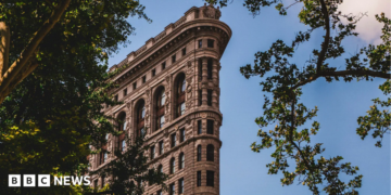 A view of the top section of the Flatiron Building, with trees surrounding it, showing its intricate Beaux-Arts detailing