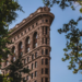 A view of the top section of the Flatiron Building, with trees surrounding it, showing its intricate Beaux-Arts detailing