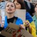 Ukrainians, including a young woman draped in a Ukrainian blue-and-yellow flag, hold placards reading 'Bring him back" during a protest against the dismissal of Defence Minister Mykhailo Fedorov in downtown Kyiv