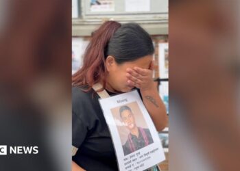 Dolma Gurung crying into her hand while holding a poster of her missing husband.
