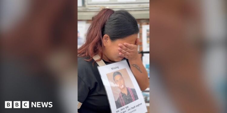 Dolma Gurung crying into her hand while holding a poster of her missing husband.