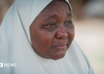 A woman wearing a white hijab, her eyes red from crying