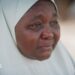 A woman wearing a white hijab, her eyes red from crying
