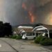 An image showing grey and orange smoke rising from behind a row of homes on a residential street in Summerland, British Columbia.