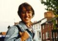A young woman smiles wearing a denim jacket and glasses in a clearly old colour picture