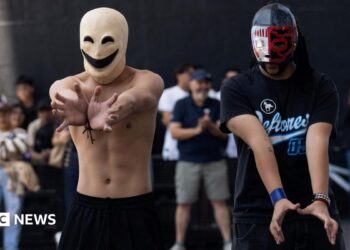 Two young men in masks hold their hands out.