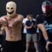 Two young men in masks hold their hands out.