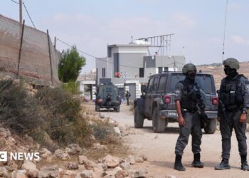 Members of the Israeli security forces stand guard near a Palestinian house, which was besieged by Israeli settlers, in Qusra
