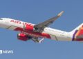 An Air India plane - white with red lettering and a red, gold and purple pattern at the tail - flying against a blue sky