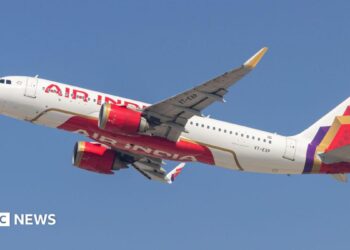 An Air India plane - white with red lettering and a red, gold and purple pattern at the tail - flying against a blue sky
