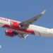 An Air India plane - white with red lettering and a red, gold and purple pattern at the tail - flying against a blue sky