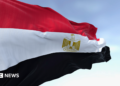 Close-up of the Egypt national flag waving. A clear blue sky is in the background.