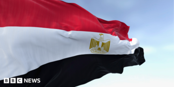 Close-up of the Egypt national flag waving. A clear blue sky is in the background.