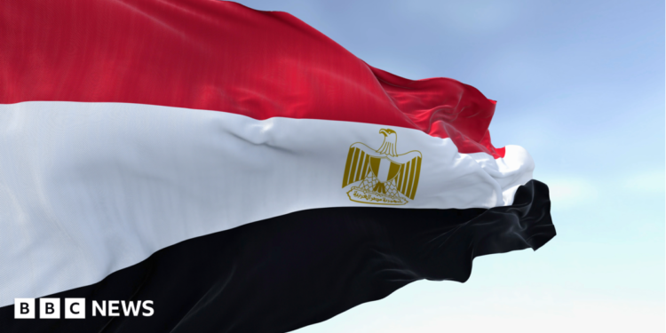Close-up of the Egypt national flag waving. A clear blue sky is in the background.