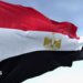 Close-up of the Egypt national flag waving. A clear blue sky is in the background.