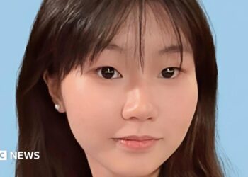 Close-up of a young Chinese girl smiling at the camera, against a blue background