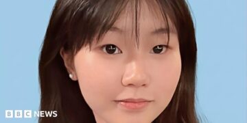 Close-up of a young Chinese girl smiling at the camera, against a blue background