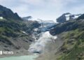 A blue lagoon underneath a white snowy glacier, framed by tall green mountains either side