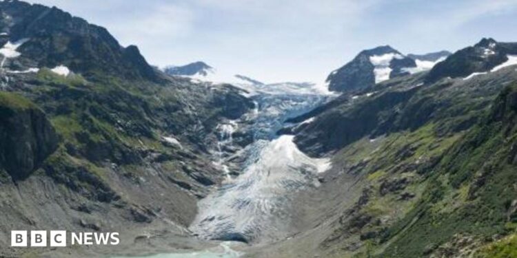 A blue lagoon underneath a white snowy glacier, framed by tall green mountains either side