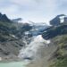 A blue lagoon underneath a white snowy glacier, framed by tall green mountains either side