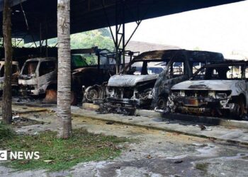 Five burned out vehicles are lined up under a tin roof structure