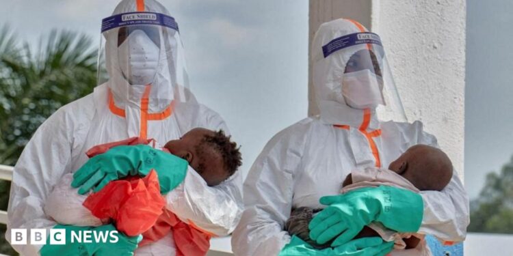 Two health workers in PPE each hold a young baby.