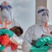 Two health workers in PPE each hold a young baby.
