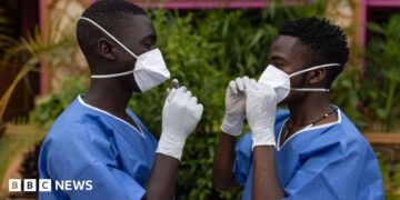 Two men wearing protective gear face each other while adjusting their masks