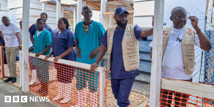 A row of men and women in medical uniforms and white wellington boots at the inauguration of a new Ebola treatment centre in Rwakole, Bunia, DR Congo.