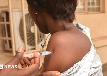 A nurse injecting the arm of a health worker in West Africa with Ervebo - archive shot