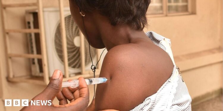 A nurse injecting the arm of a health worker in West Africa with Ervebo - archive shot