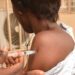 A nurse injecting the arm of a health worker in West Africa with Ervebo - archive shot