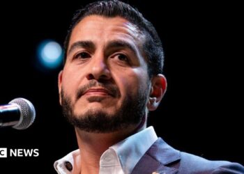 Abdul El-Sayed on stage wearing an open necked white shirt and blue suit jacked, at an election night watch party at The Majestic Theatre in Detroit