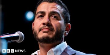 Abdul El-Sayed on stage wearing an open necked white shirt and blue suit jacked, at an election night watch party at The Majestic Theatre in Detroit