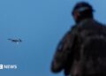 A Ukrainian soldier operating a drone, which is flying in the air in the background