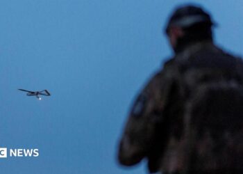 A Ukrainian soldier operating a drone, which is flying in the air in the background