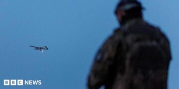 A Ukrainian soldier operating a drone, which is flying in the air in the background