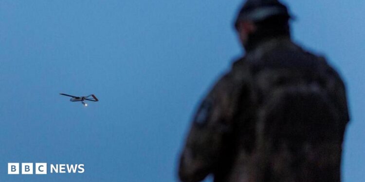 A Ukrainian soldier operating a drone, which is flying in the air in the background