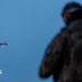 A Ukrainian soldier operating a drone, which is flying in the air in the background
