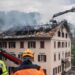 Large flames come out of the windows in the top floor of a building at night.