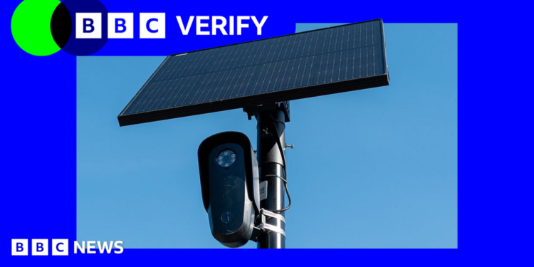 A black Flock surveillance camera attached to a pole with a solar panel attached above it