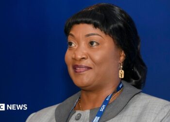 Jewel Howard-Taylor  wears a blue lanyard and grey jacket, gold earring at an economic forum in Poland, 2021. She has shiny black hair.