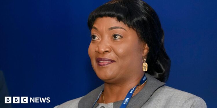 Jewel Howard-Taylor  wears a blue lanyard and grey jacket, gold earring at an economic forum in Poland, 2021. She has shiny black hair.