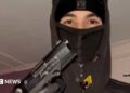 A teenager wearing a black balaclava and hoodie holding up a handgun, with his gloved hand on the trigger