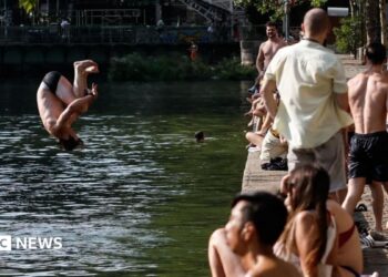 A man jumps into the water as people gather along the banks of the Canal Saint-Martin in Paris, France. Photo: 29 July 2026
