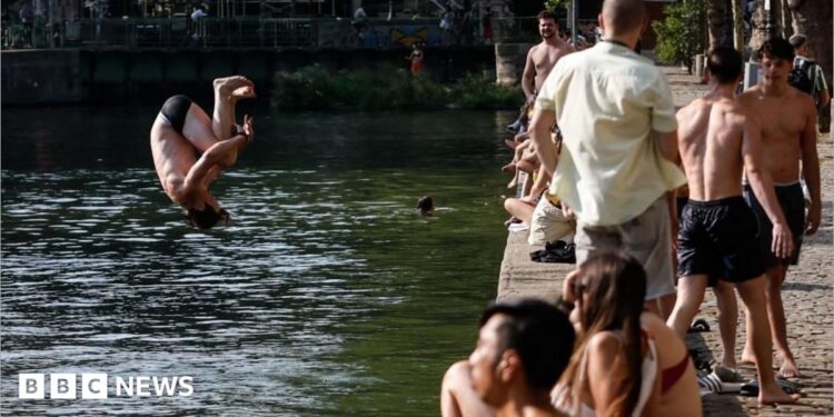 A man jumps into the water as people gather along the banks of the Canal Saint-Martin in Paris, France. Photo: 29 July 2026