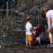 A woman and a toddler stand by charred ground and burned plants.