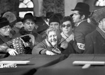 Women mourn the victims in a black and white photo showing coffins